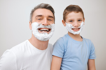 Shaving, father and child with portrait in studio for grooming, skincare lesson and teaching hygiene. Learning, mature man and boy kid with foam cream for cleaning face or support on white background