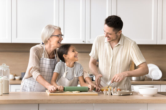Family recipe. Happy friendly 3 diverse generations relatives old grandma young adult dad little preteen child girl spend funny leisure time at modern house kitchen doing chores cooking pie for lunch