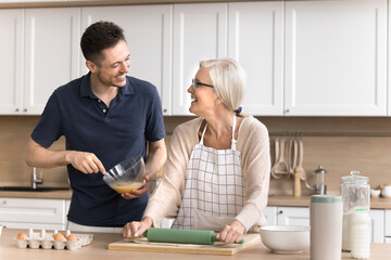 Cozy parent house. Young man loving grown up son visit elderly mom help dear mother to cook healthy...