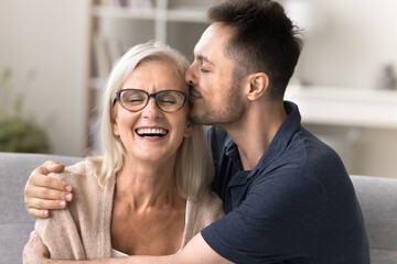 Touching care. Affectionate grateful young adult son embrace smiling elder age retired mother in...
