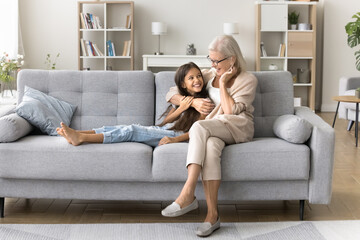 Granny is my trusted person. Happy little girl junior schoolchild relax on comfy couch at living...