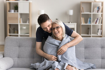 Let me take care of you. Caring attentive grown up millennial man son wrapping shoulders of...