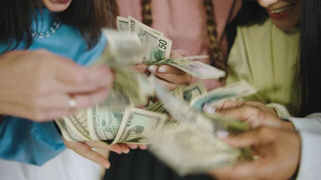Group of five multiracial female students counting money together in a modern library setting during the afternoon