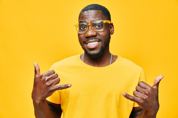Smiling young man making a call hand gesture, wearing yellow glasses and a bright yellow shirt...