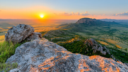 Naklejka premium Rocky mountain peak overlooking a vast green valley during a vibrant golden hour sunset.