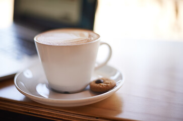 Coffee, laptop and drink in restaurant for hospitality, service and complimentary cookie. Mug, customer care and latte at cafe table for break, caffeine and cappuccino in cup with tech for networking