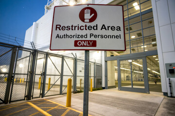 A sign indicating a restricted area, with a warning for unauthorized personnel, set in an industrial environment during dusk.