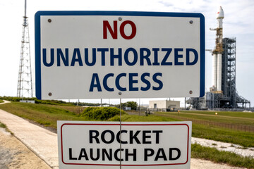 Fototapeta premium A caution sign warns against unauthorized access to a rocket launch pad, with a rocket visibly set for launch in the background.