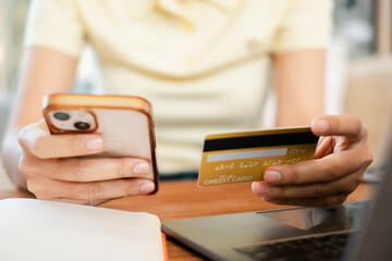 Close-up of hands holding a smartphone and credit card, illustrating online shopping and digital payment in a cozy home setting.