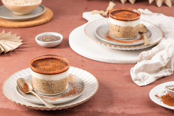 Chia pudding topped with creamy yogurt and cocoa powder, served in glass jars on elegant plates with spoons, set on a rustic table