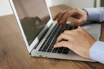 Businessman using laptop at wooden table, closeup. Modern technology