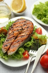Tasty grilled salmon steak with vegetables served on light grey table, closeup