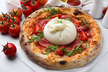 Delicious pizza with burrata cheese, arugula, tomatoes and ham on light grey table, closeup