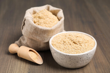 Oat bran in bowl, scoop and burlap bag on wooden table, closeup
