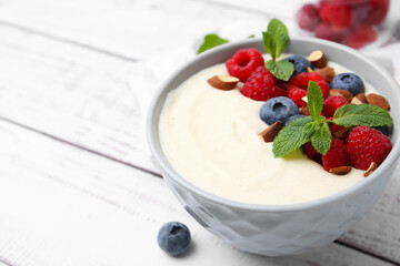Tasty cooked semolina porridge with almonds, berries and mint on white wooden table, closeup. Space for text