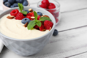 Tasty cooked semolina porridge with almonds, berries and mint on white wooden table, closeup. Space for text