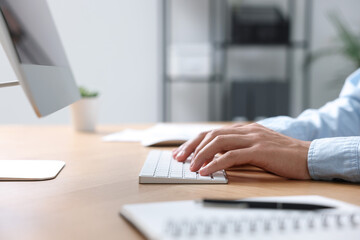 Fototapeta premium Man working on computer at wooden desk in office, closeup