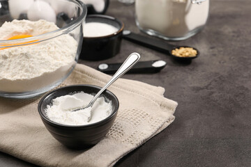Baking powder and spoon in bowl on grey textured table