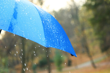Open blue umbrella under pouring rain outdoors, closeup. Space for text