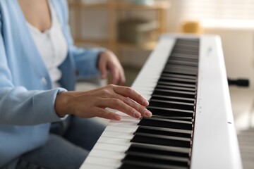 Fototapeta premium Woman playing synthesizer indoors, closeup. Electronic musical instrument