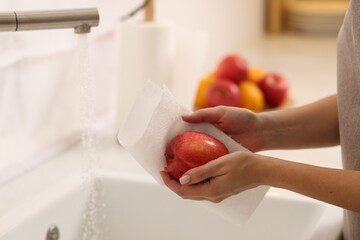 Woman wiping apple with paper towel above sink in kitchen, closeup