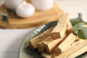 Palo santo sticks and eucalyptus leaves on white wooden table, closeup