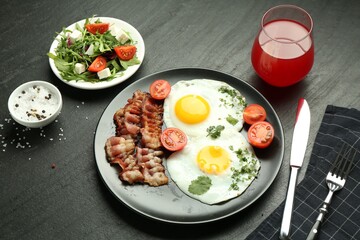 Tasty brunch. Delicious fried eggs, bacon, salad and glass of juice served on black table