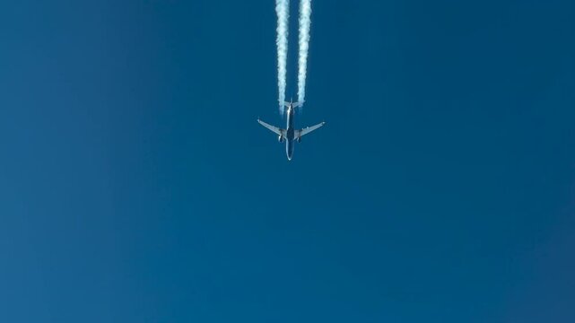 Unique aerial chasing view of the botton part of the fuselage of a white and blue jet airplane and its trail recorded from another jet flying same route bellow. 4rK
