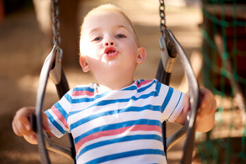 Fun, swing and portrait of kid in park with play, outdoor adventure and child development in nature. Relax, wellness and happy boy in playground for growth, morning games or playful childhood weekend