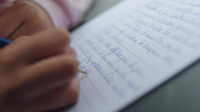 Closeup shot capturing a student writing a dictation with blue ink pen given by class teacher in school of France.