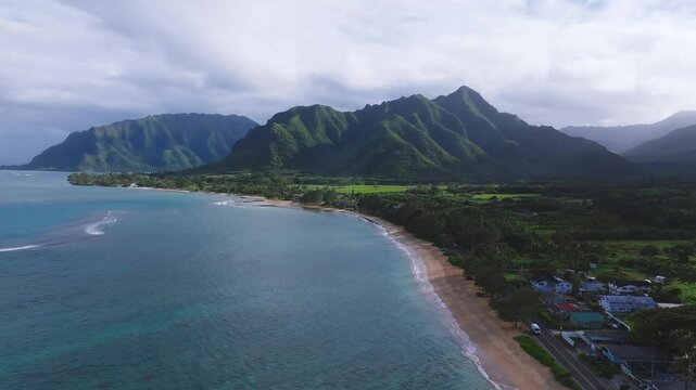 Aerial view of Oahu, Hawaii, showing turquoise waters, sandy beach, and the lush Ko olau mountain range in a smooth, sweeping motion.