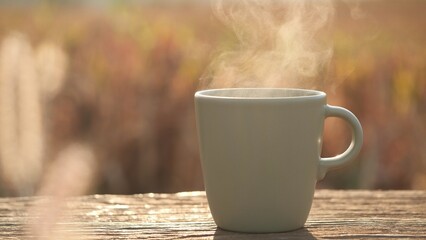 Close-up of steam rising from a coffee cup on an old wood table in the early light against an...