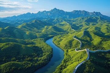 Fototapeta premium Lush green hills and winding river under clear blue sky near majestic mountain range