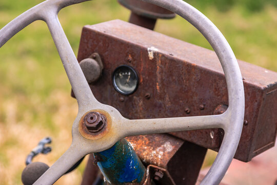 A rusted old tractor steering wheel with a gauge on the front