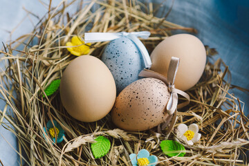 Vibrant Easter eggs are arranged in a cozy nest made of straw, with cheerful flowers contrasting against a soft blue backdrop. This scene captures the festive spirit of spring and Easter concept