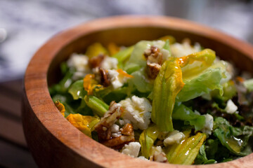 Fitness salad with zucchini blosoms, ricotta cheese and roasted pecans on a rustic wooden bowl.