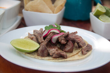 Grilled carne asada taco on a soft corn tortilla, topped with radish slices, fresh cilantro, and a...