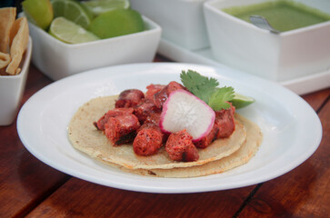 Close-up of a juicy grilled chistorra taco with radish and cilantro, highlighting the sausage, grill marks, and vibrant colors in a tropical setting.