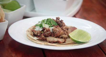 Close-up side view of a crispy fried tripe taco on a corn tortilla, garnished with onion, cilantro, and lime, served on a rustic plate.