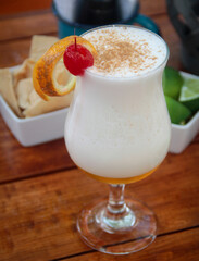 High-angle view of a layered almond liqueur cocktail with creamy foam, garnished with an orange twist and maraschino cherry.