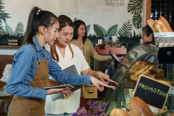 Attentive barista in blue, Smiling Asian woman in sweater enjoys ambiance of quaint coffee shop with fresh bread, embodying relaxed small business culture. small family business