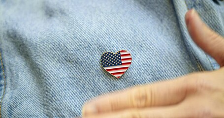 American patriot pinning shiny lapel pin in the shape of a heart with the US American flag. Celebrating patriotism and love of America for 4th of July or to celebrate another patriotic USA holiday. - Powered by Adobe