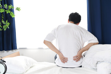 ベッドの上で腰を抑える若い男性の後ろ姿