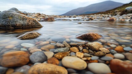 Clear stream flows over colorful pebbles, mountain backdrop, nature serenity