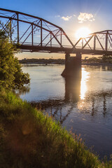 A bridge spans a river with a sun shining on the water © Scott Prokop
