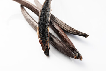 A close-up of dried vanilla pods with one split open, revealing tiny, aromatic vanilla seeds inside.