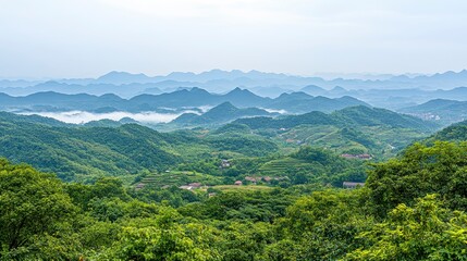 Naklejka premium Panoramic view of lush green hills and valleys on a hazy day, with a small village nestled among the vegetation. The distant mountains are shrouded