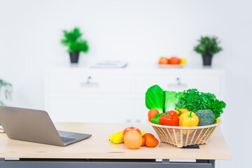 A nutritionist's table neatly arranged with a basket overflowing with fresh vegetables and fruits, including lettuce, kale, bell peppers, bananas, onions, and tomatoes, health and nutrition.