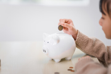 11-year-old Asian girl, wearing light brown sweater, holds piggy bank, importance of saving....
