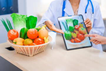 Young Asian female nutritionist in a white lab coat, working at a desk. She shows tablet with...